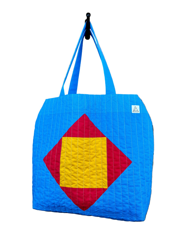 Blue quilted tote bag with geometric design hanging on a hook