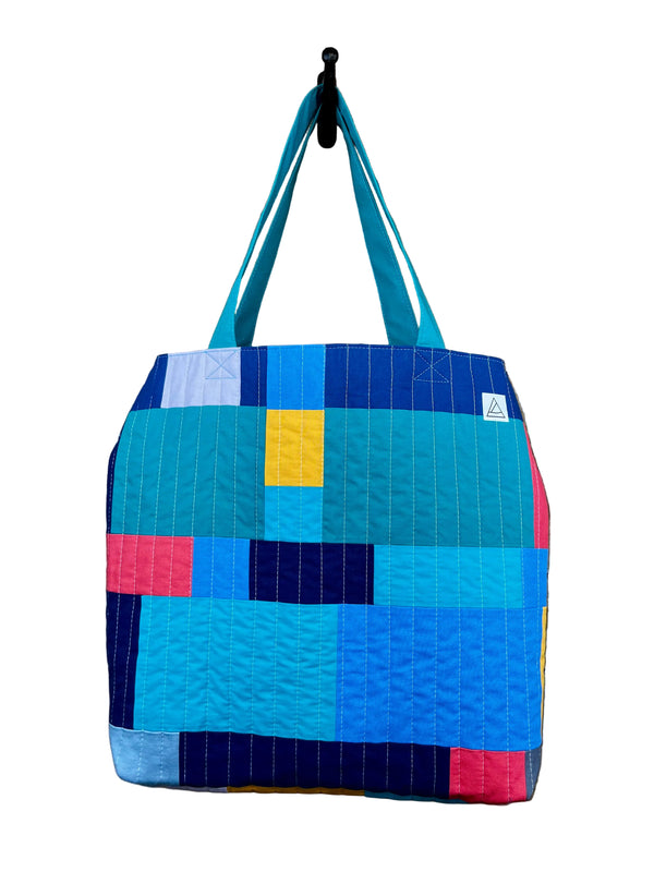 Colorful quilted tote bag with geometric pattern hanging on a hook.