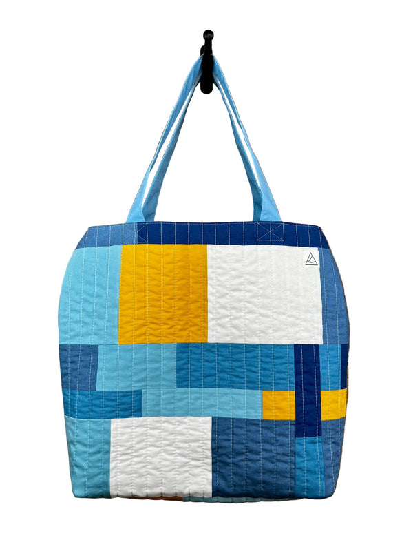 Quilted tote bag with geometric pattern hanging on a hook.