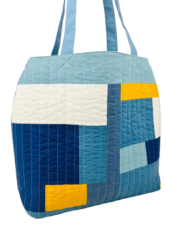 Quilted tote bag with blue, white, and yellow patchwork design on a white background