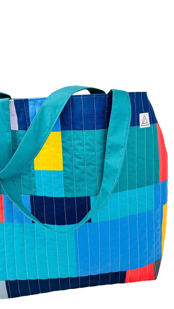 Colorful quilted tote bag with geometric pattern on a white background