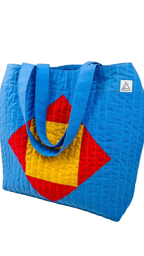 Blue quilted beach bag with red and yellow geometric design on a white background