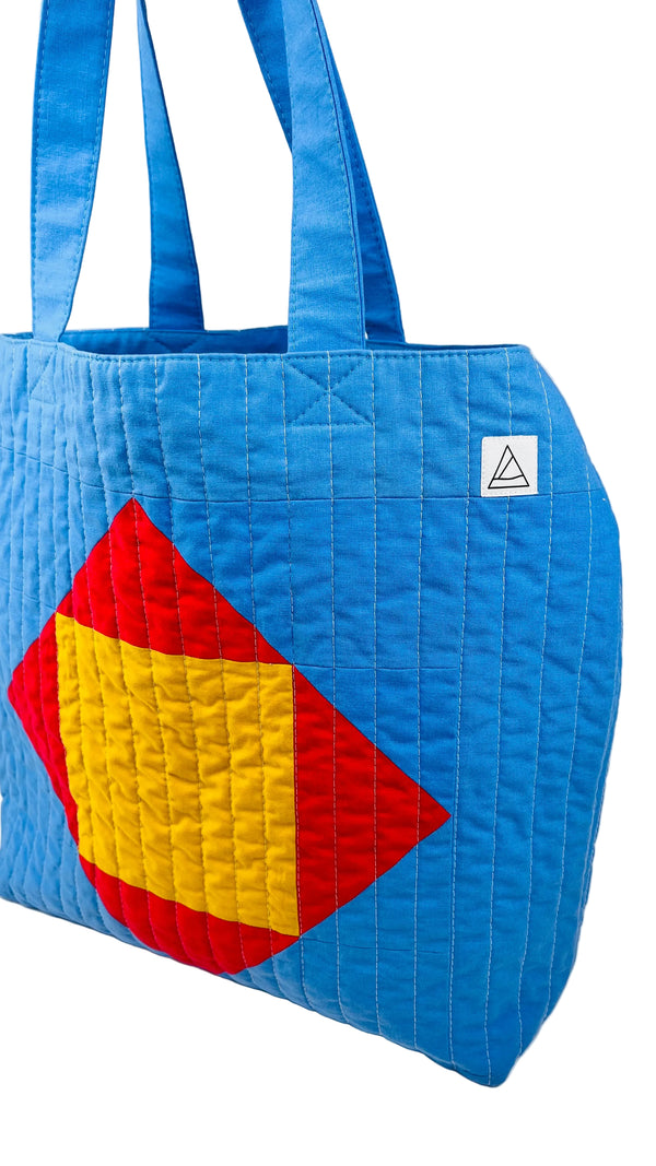 Blue quilted beach bag with red and yellow geometric shapes on a white background