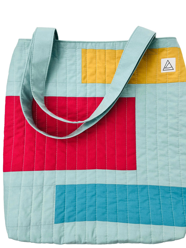 Colorful quilted tote bag with geometric pattern on a light gray background