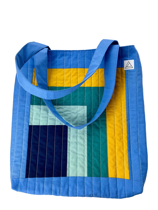 Colorful quilted tote bag with blue handles on a white background