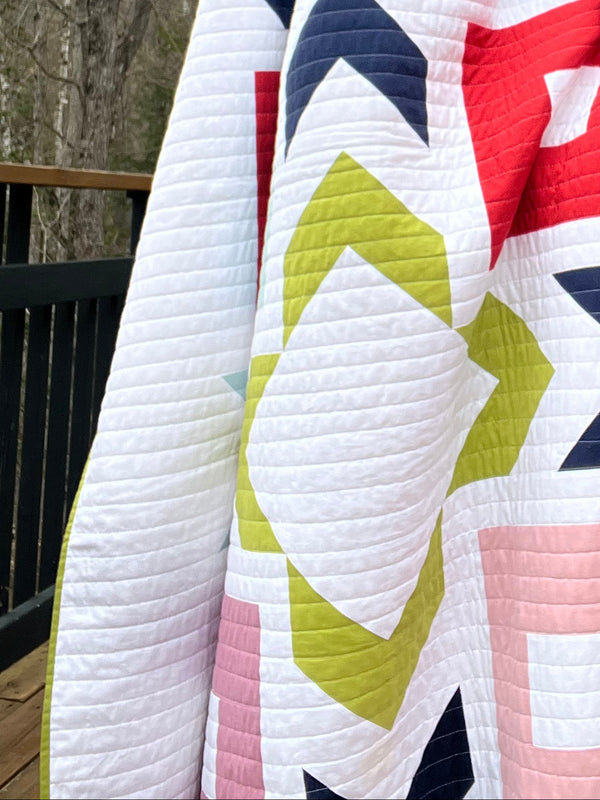 Person holding a colorful quilt outdoors with trees in the background