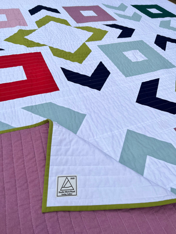 Colorful geometric quilt with a visible brand label on a purple fabric background