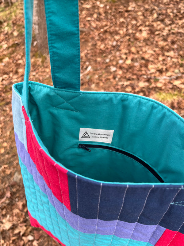 Close-up of a colourful bag with a visible brand label on a textured ground.