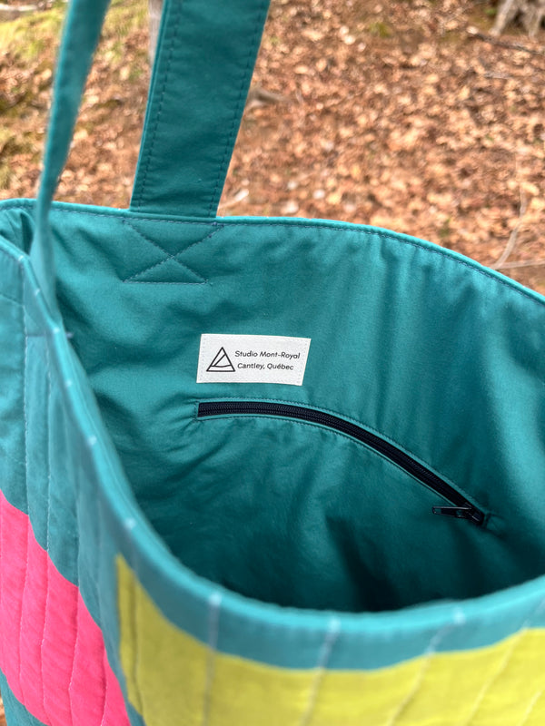 Close-up of a teal bag with a visible brand label against a blurred natural background