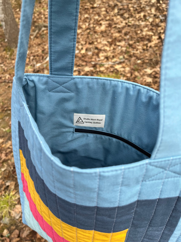 Blue quilted tote bag with colorful stripes on a natural background