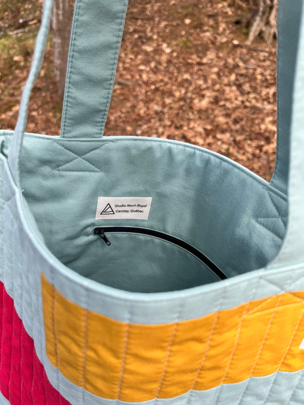 Colourful quilted bag with a brand label on a blurred natural background